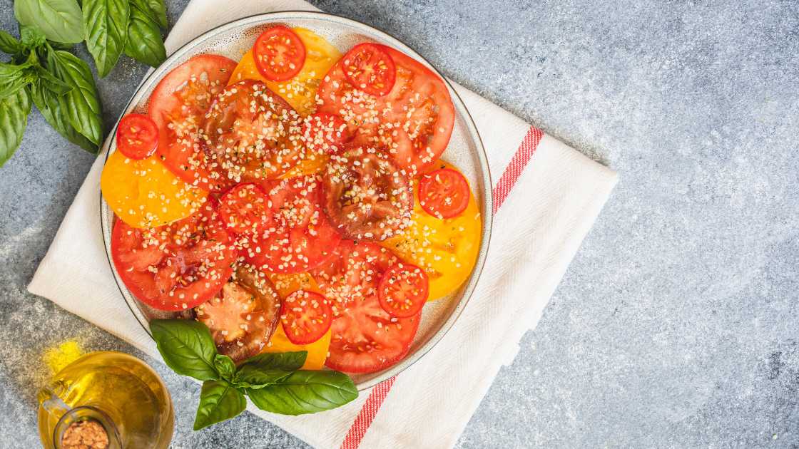 Slices of tomatoes on plate with hemp seeds sprinkled on top 