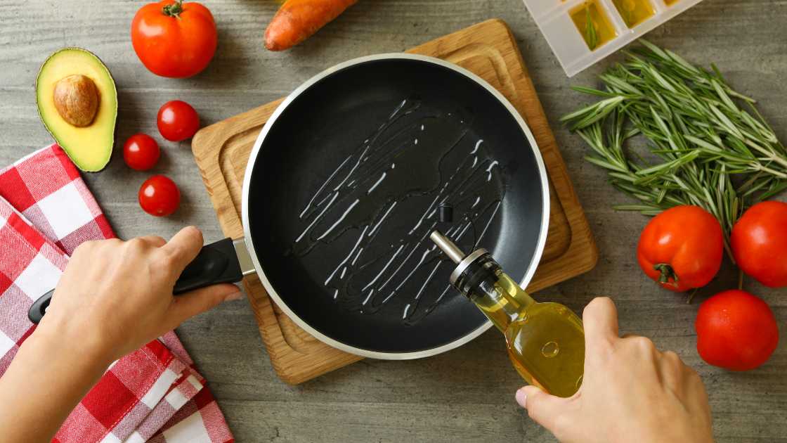 Oil being poured over frying pan on table with vegetables surrounding